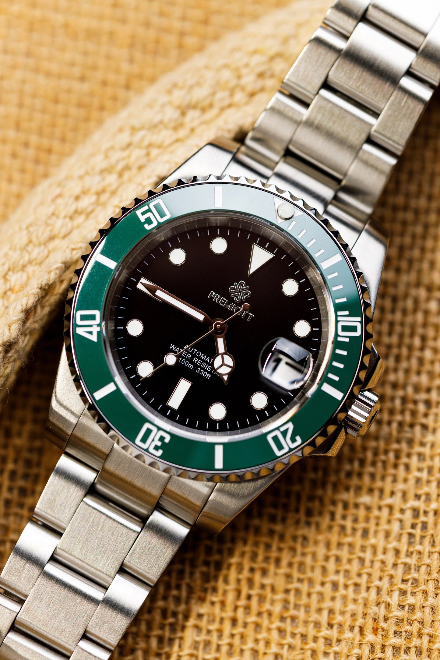 The Mariner cu cadran verde, bezel auriu și brățară din oțel inoxidabil, fundal din pânză de iută
