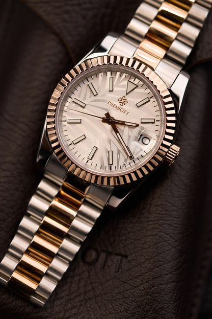 The Just Date, cadran deschis cu model de frunze de palmier, carcasa bicolora din aur roz, asezat pe piele maro.