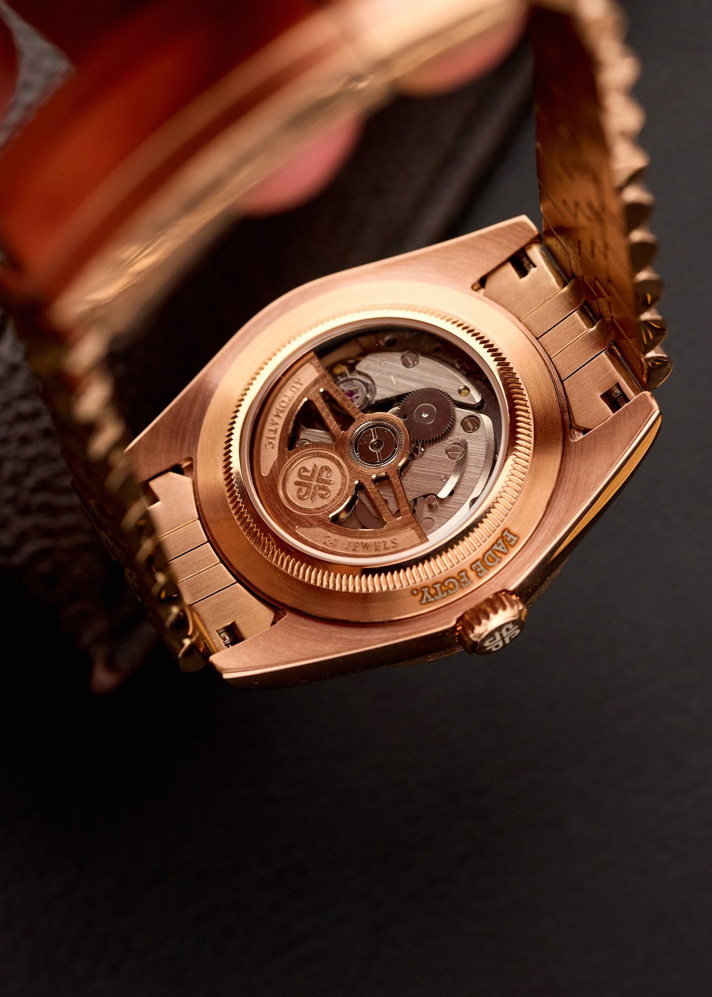 The Just Date, ceas automatic personalizat cu spate transparent aur roz, mecanism vizibil, pe fundal cu material rosu.