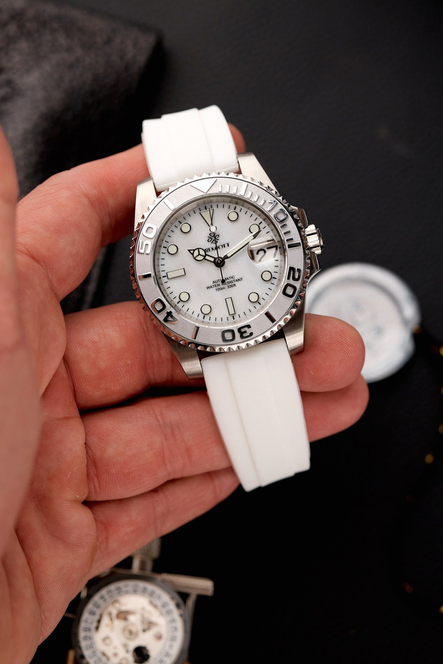 The Mariner cu cadran alb sidefat, bezel ceramic alb și curea din cauciuc alb, ținut în mână