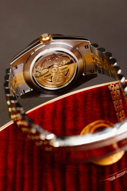The Just Date, spate transparent din aur cu mecanism automatic, inclinat intr-o cutie captusita cu matase rosie.