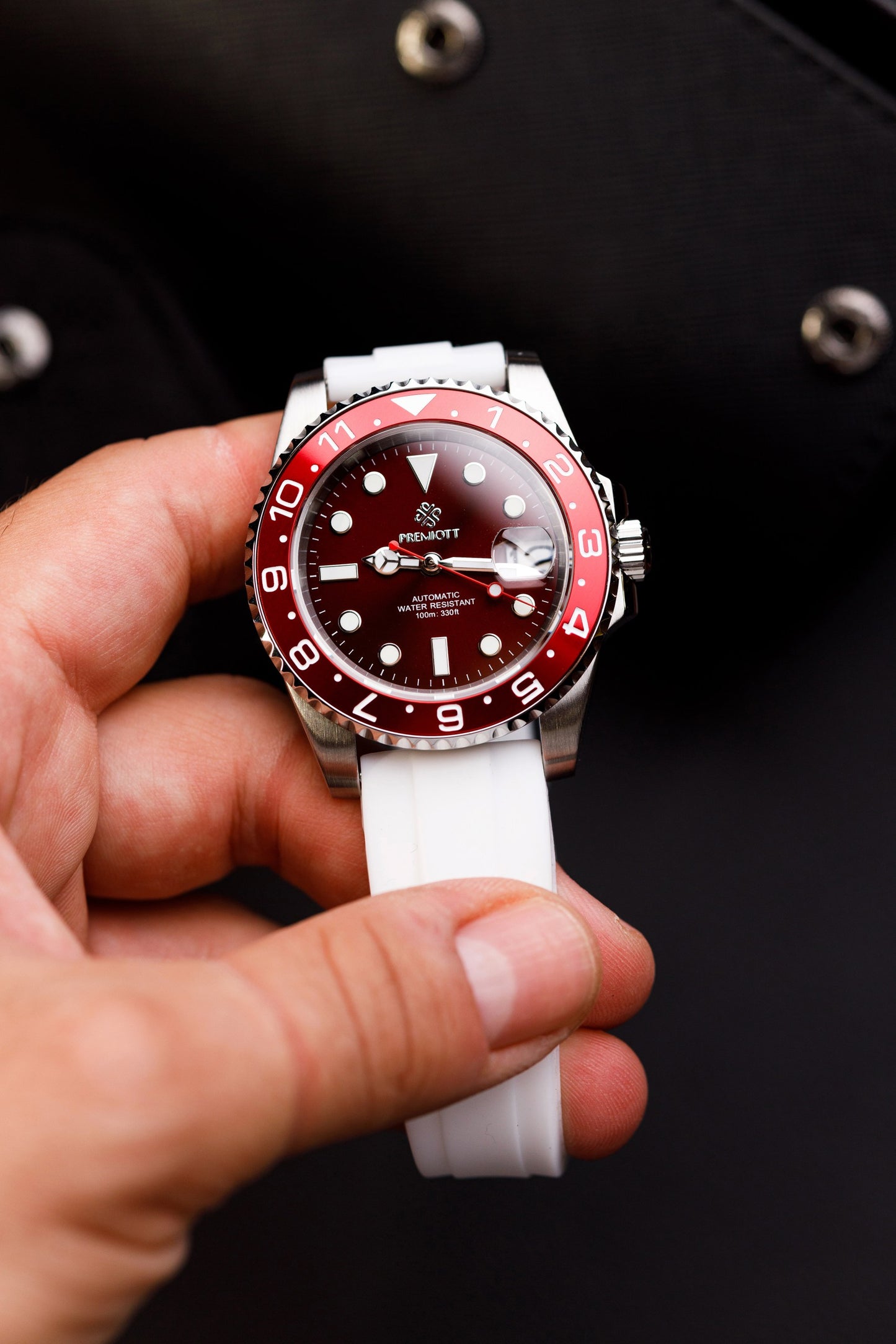 The Mariner stil GMT cu cadran bordo, bezel roșu-alb și curea din cauciuc alb, ținut în mână